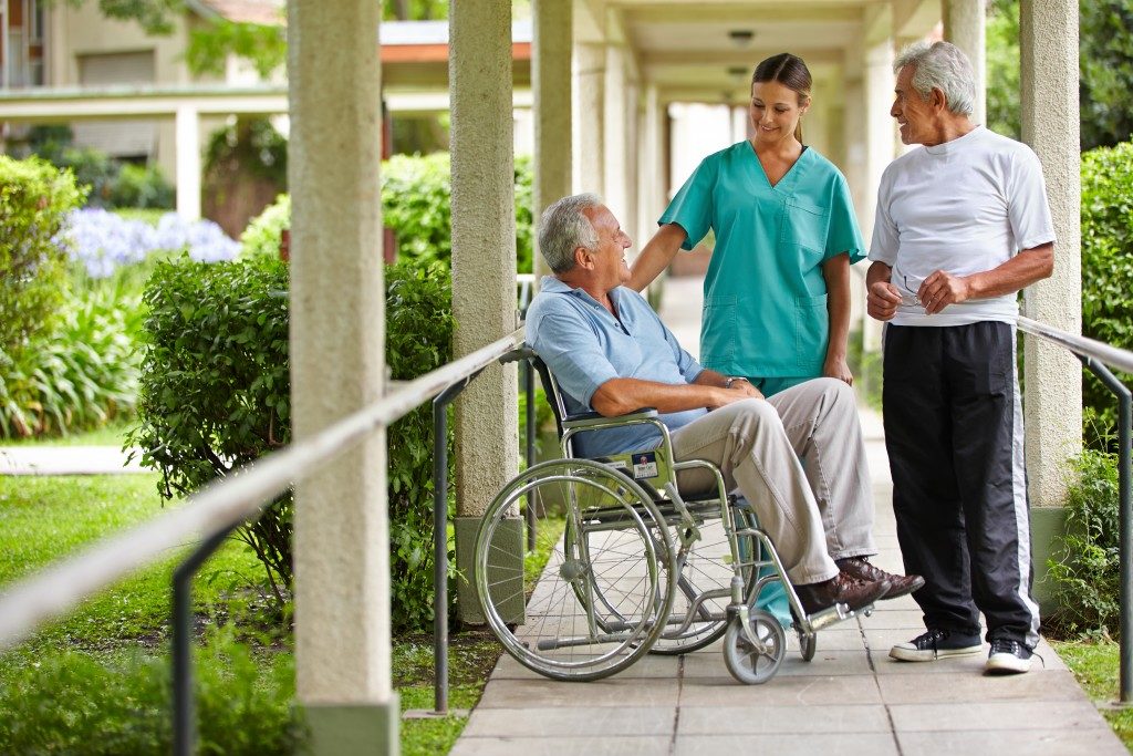 Two senior citizens talking to a nurse in a hospital garden