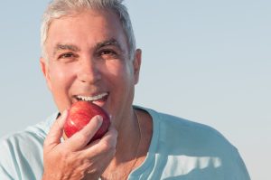 Mature man eating an apple outside the house.