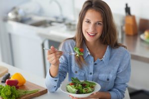 a healthy beautiful woman smiling while eating leafy salad in the kitchen
